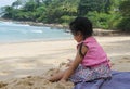 Side view of little cute girl dress casually sitting on the beach playing sand. Holiday, family, healthy child concept Royalty Free Stock Photo