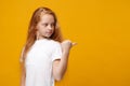 Side view of little ginger kid girl 12-13 years old in white t-shirt isolated on yellow wall background children studio Royalty Free Stock Photo