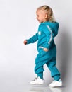 Side view of a little girl in a blue warm jumpsuit walking along the wall. Royalty Free Stock Photo