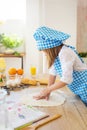 SIDE VIEW: Little girl in a cook clothes sculpts a dough on a table