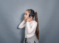 Side view little girl in headphones. White T-shirt, gray sweatpants. Holds headphones, listens to music Royalty Free Stock Photo