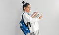 Side view of a little girl wearing uniform, backpack, and transparent eyeglasses holding pile of books on her arms. Schoolgirl Royalty Free Stock Photo