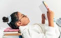 Side view of a little girl wearing uniform and transparent eyeglasses reading a book while lying on  pile of books. Schoolgirl Royalty Free Stock Photo