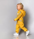 Side view of a little girl in a blue warm jumpsuit walking along the wall. Royalty Free Stock Photo