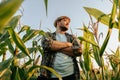 Side view looking away handsome young farmer man standing in cornfield with arms crossed, at sunset