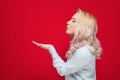 Side view of lovely young woman send kiss to you, isolated on red background. Beautiful lovely girl kissing and showing her palm Royalty Free Stock Photo