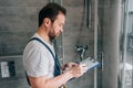 Side view of male plumber making notes in clipboard while checking shower