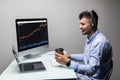 Side view of male trader with coffee cup using multiple computer screens while communicating through headphones at desk Royalty Free Stock Photo