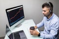 Side view of male trader with coffee cup using multiple computer screens while communicating through headphones at desk Royalty Free Stock Photo