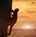 Side view of man in black climbing on rock without safety harness over sea in twilight. Recreational activity in nature