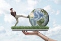 Side view of man in casual clothes kicking Earth globe, on top of digital tablet screen covered with green grass, held Royalty Free Stock Photo