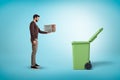 Side view of a man in a casual outfit standing near an open trash can and holding a little old-fashioned TV set. Royalty Free Stock Photo