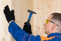 Side view of a man in construction clothes and goggles nails the board with nails and a hammer Royalty Free Stock Photo