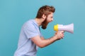 Side view of man holding megaphone near mouth, loudly speaking, screaming, making announcement. Royalty Free Stock Photo