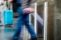 A man with a rolling carry-on luggage passing through stainless steel ticket gates with motion blur