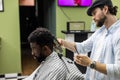 Side view of serious man with stylish modern haircut looking forward in barber shop. Hand of barber keeping razor and cutting hair Royalty Free Stock Photo