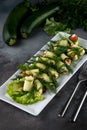 Side view many stuffed zucchini rolls with meat and vegetables on a white plate on grey cement background with cutlery, concept of