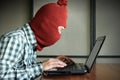 Side view of masked hacker wearing a balaclava looking a laptop and stealing important information data. Network security and priv Royalty Free Stock Photo