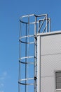 Side view of metal vertical access ladders with round safety tunnel for use as emergency fire escape on side of industrial