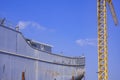 Metal vessel hull during maintenance work in dry dock with tower crane against blue sky in shipyard area Royalty Free Stock Photo