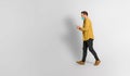 Side view of mid adult man wearing yellow jacket and protective face mask using smart phone while walking isolated against white Royalty Free Stock Photo