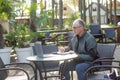 Side view of middle-aged man wearing black jacket, sitting at table in cafe, writing notes in notepad looking at laptop. Royalty Free Stock Photo