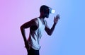 Side view of millennial black athlete in VR headset running in neon lighting. Contemporaty technologies in sports