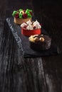 Side view on mini party tartlets with fresh fruit, chocolate, nuts and cream on black slate background