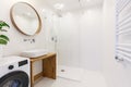 Side view of a modern bathroom interior with a shower, wash basin, round mirror, washing machine and wall radiator Royalty Free Stock Photo