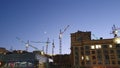 A side view of a modern buildings with construction cranes on the background with blue sky in twilight