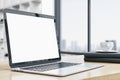 Side view of modern designer office desktop with empty white mock up laptop screen, coffee cup and other items on blurry office Royalty Free Stock Photo