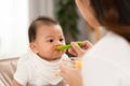 Side view mother feeding her asian baby daughter with pumpkin mashed or vegetable mash on rubber spoon.Mom trying to feed little Royalty Free Stock Photo