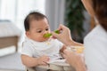 Side view mother feeding her asian baby daughter with pumpkin mashed or vegetable mash on rubber spoon.Mom trying to feed little Royalty Free Stock Photo