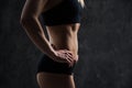 Side view of muscular fitness female model standing on black background. Young woman wearing sports bra looking down in Royalty Free Stock Photo