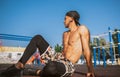 Side view of muscular young male relaxing on sports ground outdoors. Handsome athlete man looking away sitting on the ground. Royalty Free Stock Photo