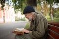 Side view of old homeless man with long grey hair reading a book.