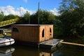 Side view of older wooden square house boat on floating platform with white modern motor boat anchored on the left