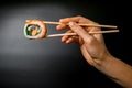 side view of one appetizing Philadelphia roll hand holding with bamboo chopsticks on dark background Royalty Free Stock Photo