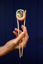 side view of one Philadelphia roll in hand holding with bamboo chopsticks on dark background Royalty Free Stock Photo