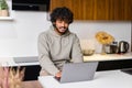 Side view at optimistic Indian man wearing hoodie sitting at desk and using laptop Royalty Free Stock Photo