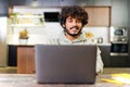 Side view at optimistic Indian man wearing hoodie sitting at desk and using laptop Royalty Free Stock Photo