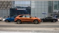 Side view of orange Porsche Macan fast moving on winter city road. Car rushing on snowy street. Premium SUV driving along urban Royalty Free Stock Photo