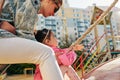 Side view outdoor image of happy playful little girl climbing on a rope at playground. Mother helping her daughter to climb on a Royalty Free Stock Photo