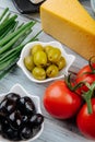 side view of piece of dutch cheese with green onion, pickled olives and fresh tomatoes on grey wooden background