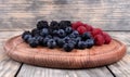 Side view of a pile of ripe red, blue and black berries laying in wooden plate Royalty Free Stock Photo