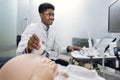 Side view of pleasant smiling African American male doctor doing ultrasound scan for unrecognizable pregnant woman in Royalty Free Stock Photo