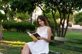 Side view of pleased brunette woman sitting on the bench and reading a book in the park Royalty Free Stock Photo