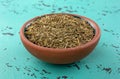 Side view of a portion of organic thyme leaf in a small bowl atop a green and black mottled countertop