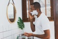 Side view portrait of african American man look in mirror apply cream or foam shaving on beard in bathroom. Young man perform Royalty Free Stock Photo