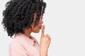 Side view portrait of African American young woman wears pink shirt, holding index finger on lips, asking to keep silence. Dark Royalty Free Stock Photo